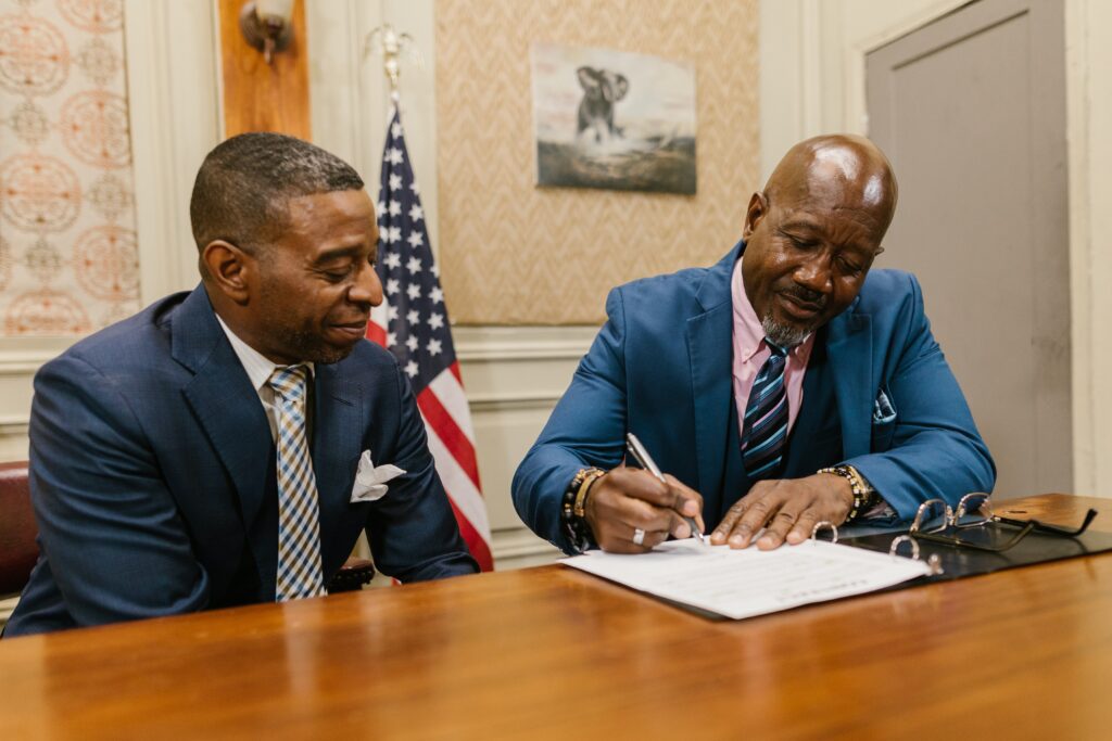 Two black businessmen smiling as one signs a contract